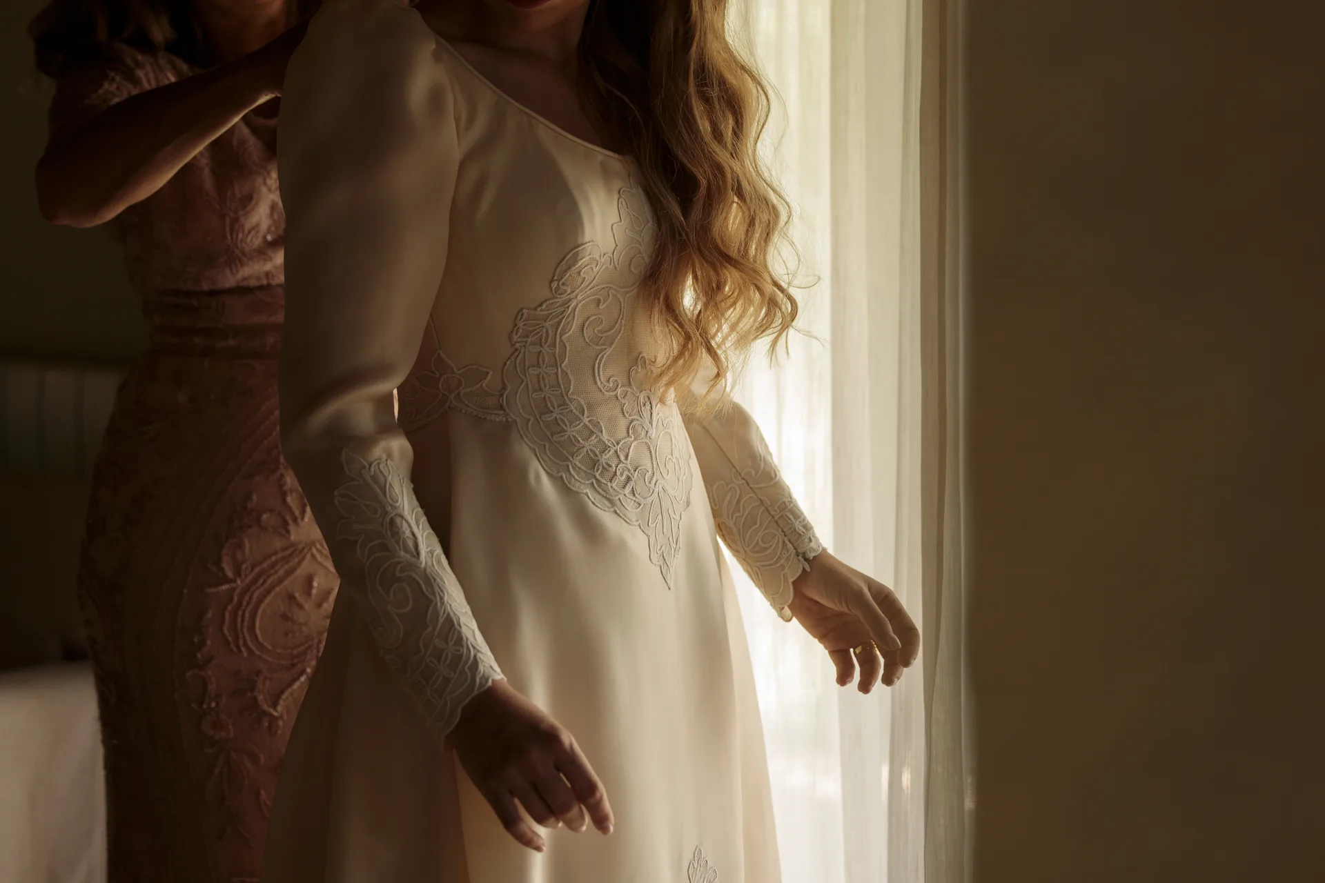 The bride gets ready by a window before the celebration