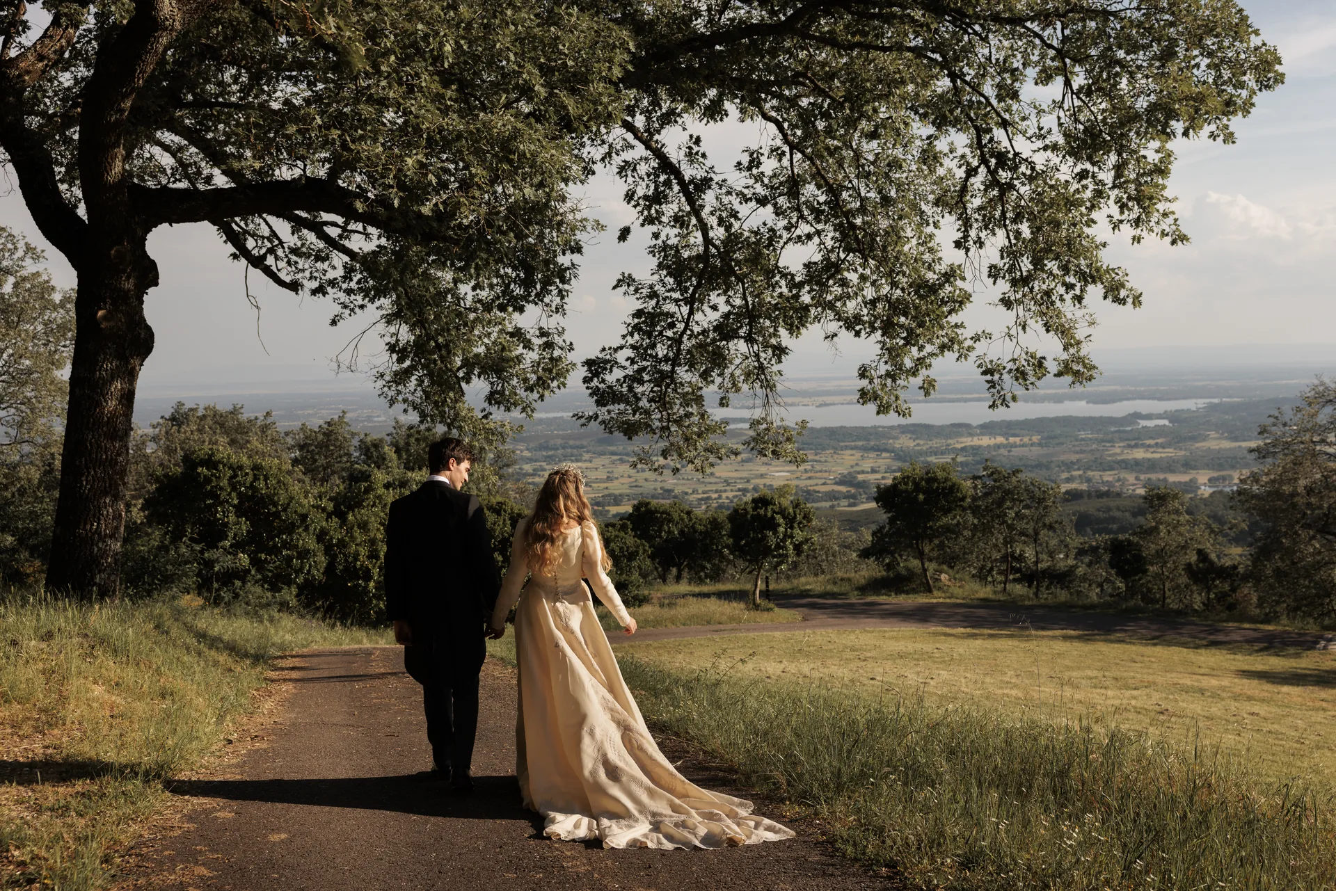 The couple walk along a path on the estate with the valley behind them